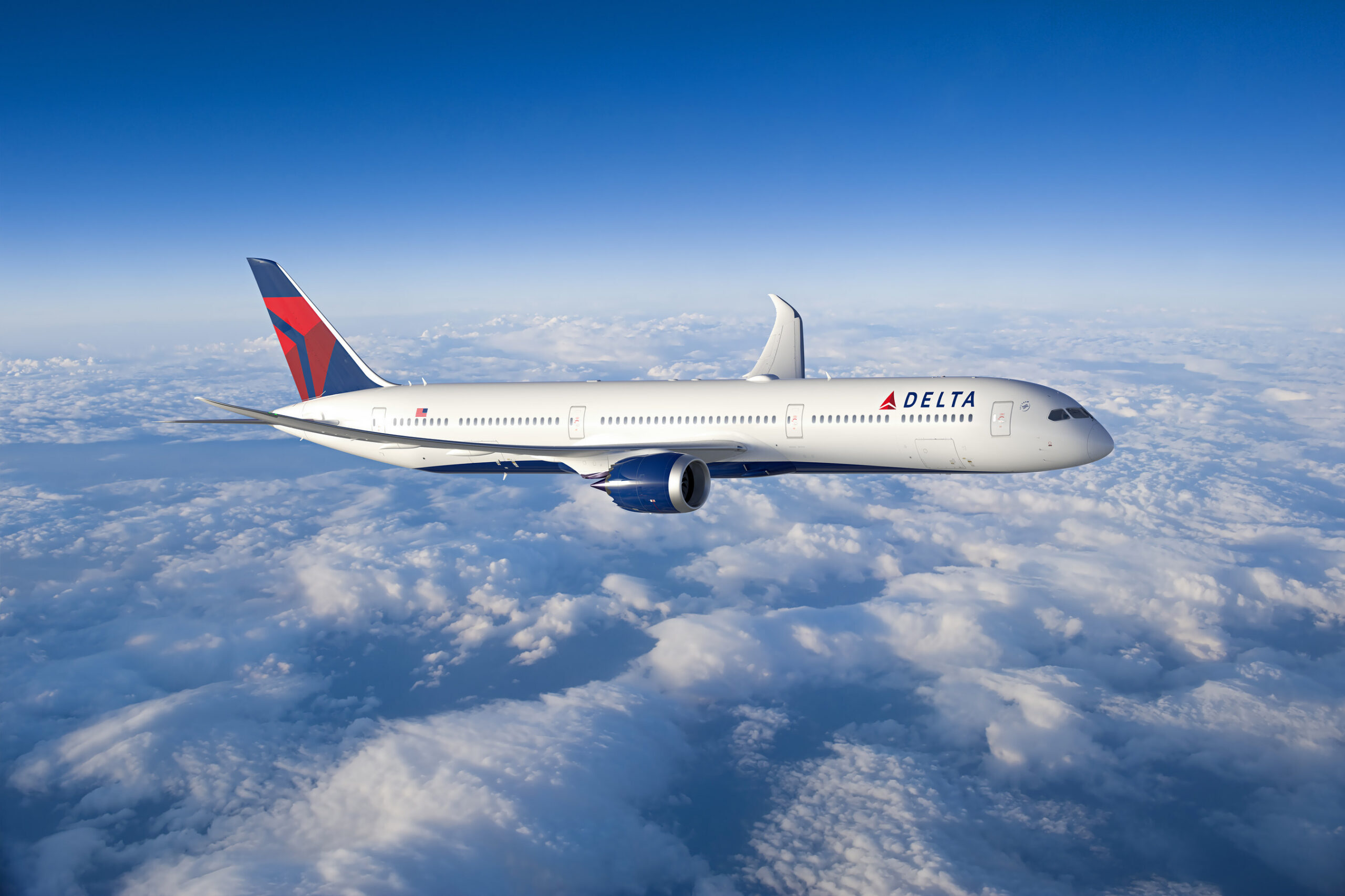 A Delta Air Lines airplane is flying above the clouds. The aircraft is white with the Delta logo on the fuselage and a red and blue tail. The sky is clear and blue.
